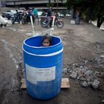 A little girl stands inside a plastic barrel while her family waits to collect water from an open pipe above the Guaire River, during rolling blackouts which affect the water pumps in people's homes, offices and stores, in Caracas, Venezuela.<br/>(Ariana Cubillos/AP/Shutterstock)